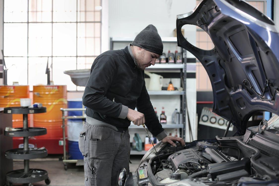 Free Mechanic checking a car engine in a garage, ensuring quality maintenance and repair. Stock Photo